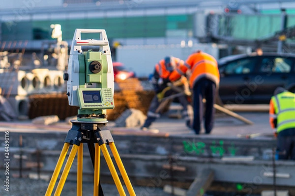 Fototapeta Surveyor equipment (theodolite) on construction site of the airport, building or road with construction machines in background