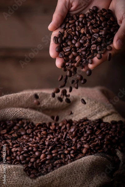 Fototapeta Crop close-up view of hands with coffee beans pouring to sack