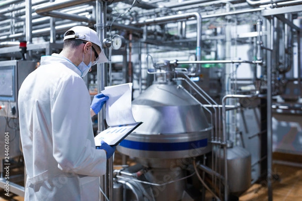Obraz technologist taking necessary notes while standing at production department of dairy factory