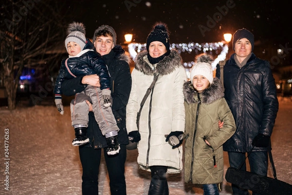 Fototapeta A good family of five people, two adults and three children have a rest, walk, have fun, spend family time in the winter night city