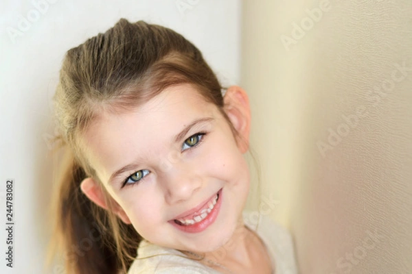 Obraz portrait of a little caucasian white beautiful brunette girl with pony tail on neutral background. smiling toothless green eyed happy girl with cute protruding ears. Kid expression portrait with fun h