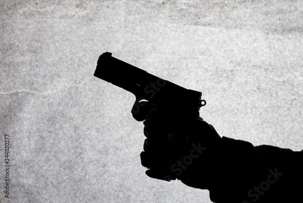 Fototapeta The gun in the hand of men who is ready to shoot at his victim. Breaking the law and crime. Attack with a weapon. Suluet on a light background.