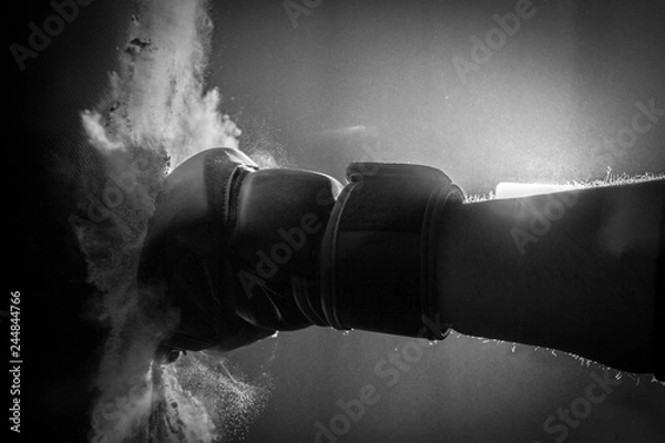 Fototapeta Moody Black & White Close Up Action Photo of a Boxing Glove Hitting a Punching Bag - with an Explosion of Dust on Contact in a Foggy, Shadowy Room