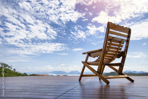 Obraz old rocking chair by wood on wood floor. in front of the chair is Seasacpe, small mountain and small island, shot by low angle from subject. In a midday.