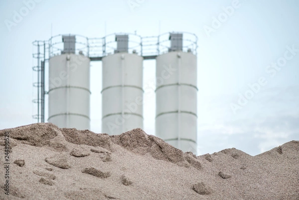 Obraz Large piles of construction sand and gravel used for asphalt production and building. Limestone quarry, mining rocks and stones. Factory in the background. Empty space for text of logo  