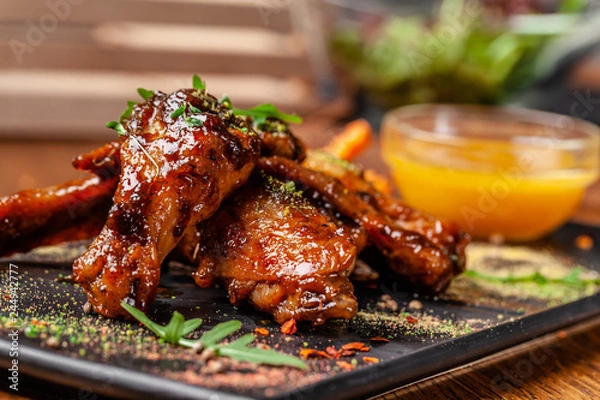 Obraz The concept of Indian cuisine. Baked chicken wings and legs in honey mustard sauce. Serving dishes in the restaurant on a black plate. Indian spices on a wooden table. background image.
