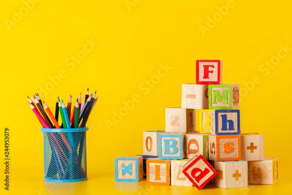 Obraz Kolorowe drewniane klocki i kubek z kolorowymi kredkami na żółtym tle