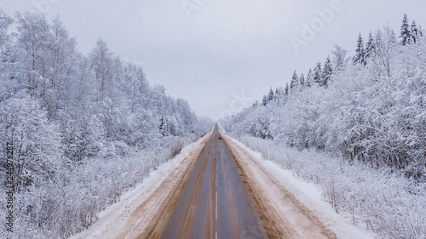 Fototapeta Aerial view of forest covered with snow, road in winter time