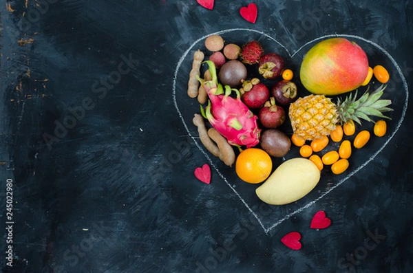 Obraz Heart from exotic tropical fruits on dark background. Pineapple, mango, passion fruit, tamarind, granadilla, kumquat, lychee, pitahaya, rambutan. Flat lay.
