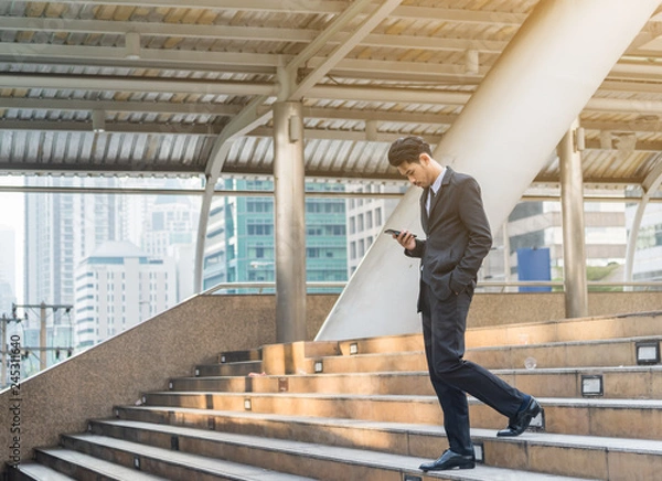 Obraz Young business people using cell phone walking ,standing separate discussion meeting on path outside office before starting work in their office.Outdoor city Business communication lifestyle concept.