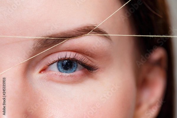 Fototapeta Cosmetologist plucks client eyebrows by thread. Close up