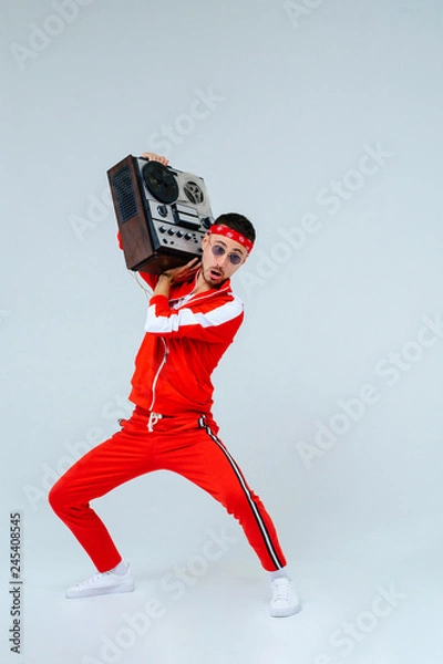 Fototapeta cheerful fashionable man wearing a red sports suit dancing jumps with a retro tape recorder. interesting and fervent style of the 90s