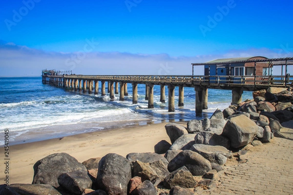 Obraz Pier on the Atlantic Ocean in Swakompund, Namibia. Beautiful pink sand, waves and stones on a sunny bright day.