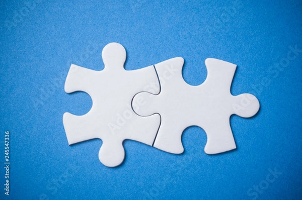 Fototapeta Closeup of Two connected jigsaw puzzle pieces on blue  background. The concept of finding the right solutions in teamwork.