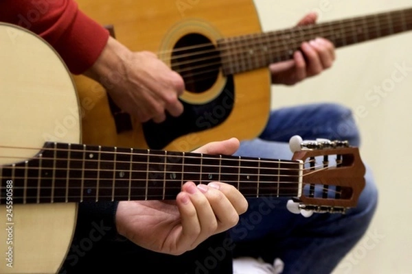 Fototapeta Closeup at left hand of guitarist learning how to play acoustic guitar instrument of traditional Greek music of "rempetika" as also jazz blues rock and roll from teacher maestro at the background