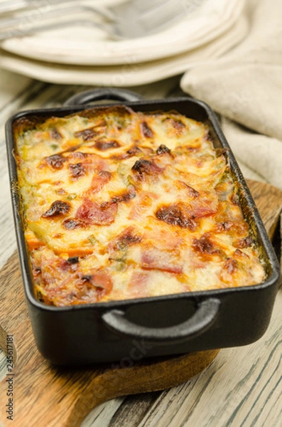 Fototapeta Potato gratin with parmesan cheese, cream and cured bacon from South Tyrol. Tartiflette: baked potatoes with bacon and cheese close up. Scalloped potato casserole 