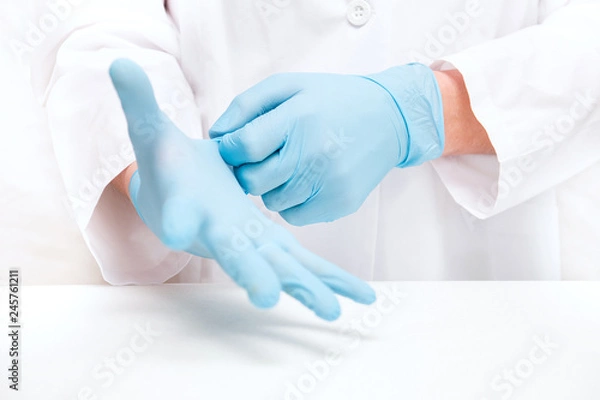 Fototapeta man-doctor wears medical gloves on while standing against a white background