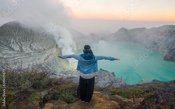 Fototapeta Back view of young woman standing on the crater of Kawah Ijen volcano in East Java, Indonesia.