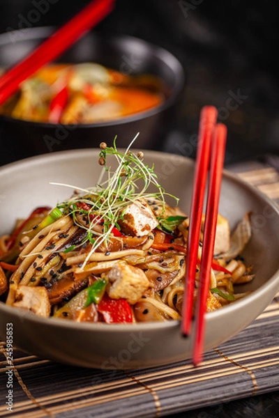 Obraz The concept of Japanese cuisine. Chinese noodles with chicken, grilled vegetables, and tofu in unagi sauce. Serving Asian dishes in the restaurant in a plate on a bamboo mat. Top view, copy space