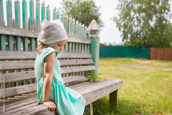 Fototapeta little girl sitting on a bench in the park