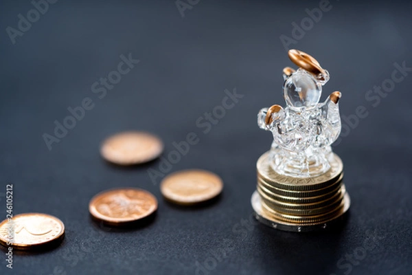 Obraz Glass angel figure over coins column on black background