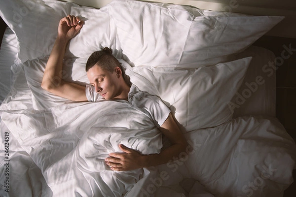 Obraz Top view - a young man is sleeping in his bed under the rays of the morning sun. The concept of early awakening and good mood for the whole day