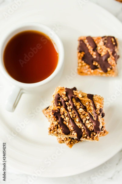 Fototapeta Granola bar with date caramel and chocolate. Healthy sweet dessert snack. Cereal granola bar with nuts, fruit and berries on a white marble table. Top view. A cup of coffee.