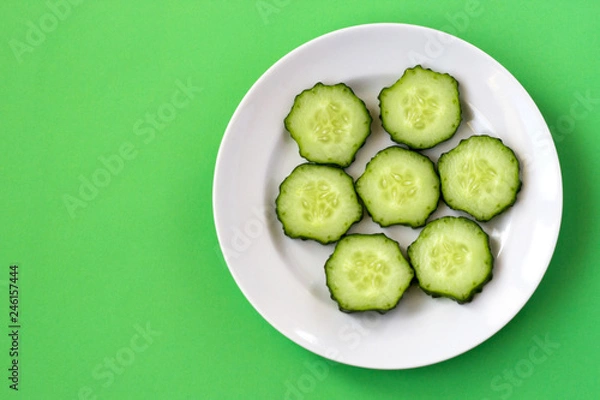 Fototapeta Top view of a plate with sliced cucumber slices on a green background.