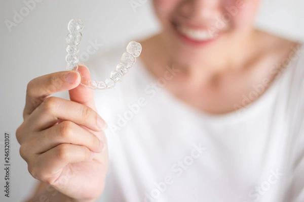 Obraz A smiling woman holding invisalign or invisible braces, orthodontic equipment