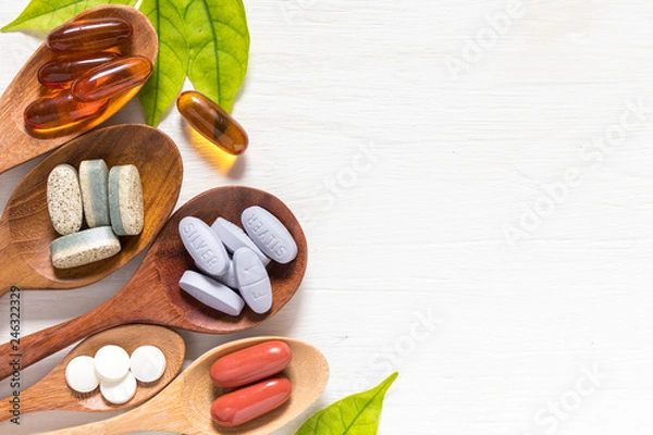 Obraz Variety of vitamin pills in wooden spoon on white background with green leaf, supplemental and healthcare product, flat lay surface