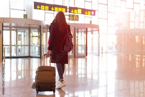 Obraz Rear view of brunette woman exit from airport with trolley (hand luggage)
