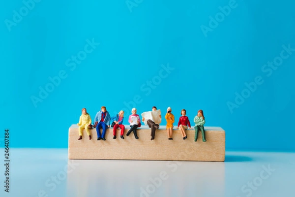 Fototapeta Miniature people sitting on wooden block with on blue background using as business and social concept