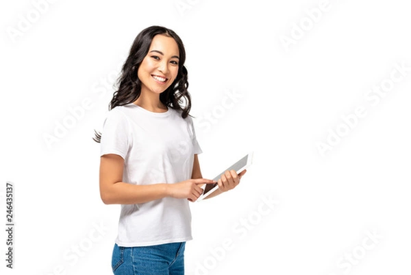 Obraz Smiling asian using digital tablet while looking at camera isolated on white
