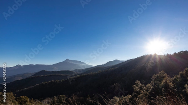Obraz Sun shining over a solid blue sky on a mountain landscape