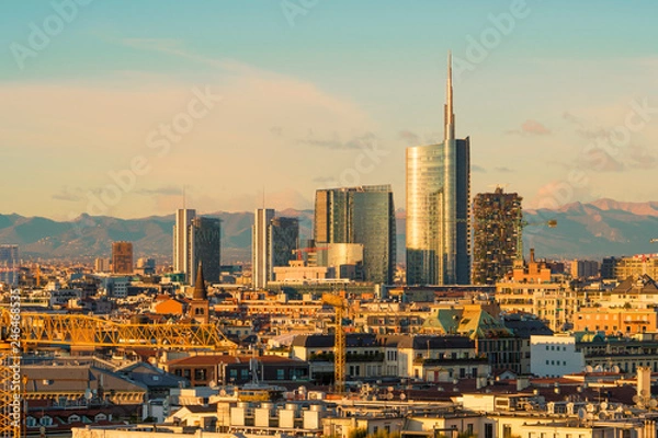 Fototapeta Milan (Italy) skyline at sunset with modern skyscrapers in Porta Nuova business district. Panoramic view of Milano city. The mountain range of the Lombardy Alps in the background.