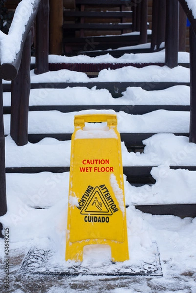 Fototapeta Sign cautiously slippery floor on a street in winter near the stairs. Red text.
