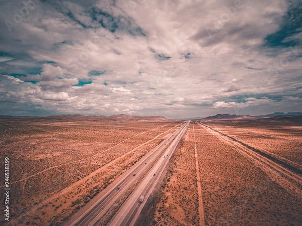 Fototapeta aerial drone shot of a highway traveling off into the distance with cars and vehicles into the blue skies with clouds and mountains