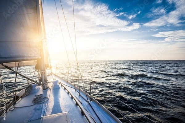 Obraz White yacht sailing at sunset. A view from the yacht's deck to the bow and sails. Baltic sea, Latvia