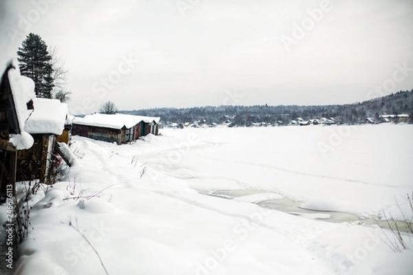 Fototapeta Frozen river covered with ice and snow in the village at winter.