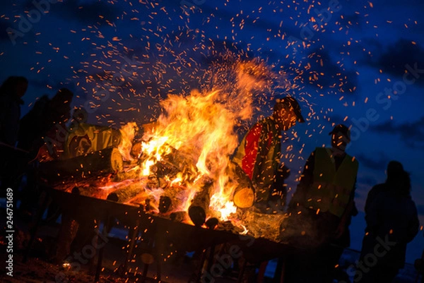 Obraz Large burning bonfire with soft glowing flame and sparkles flying all around. Romantic summer evening, people relaxing and enjoying calmness at the seaside during the Night of ancient lights.  