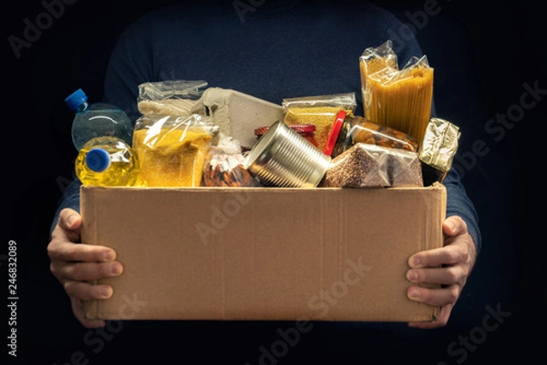 Fototapeta Mężczyzna trzyma pudełko darowizn różnych produktów na ciemnym tle