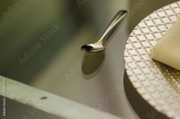 Fototapeta close up of a chrome spoon with a silver plate on one side on a transparent glass table