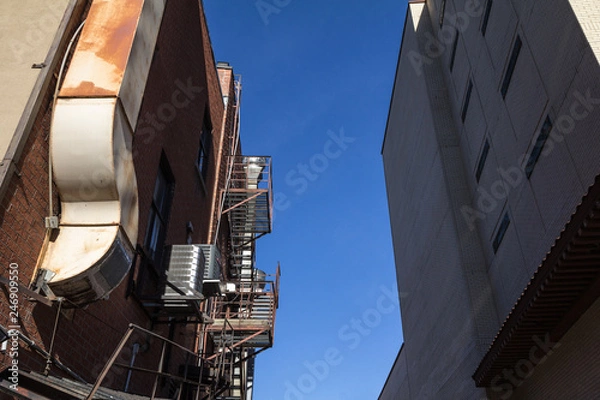 Fototapeta Fire escape rusty stairs and ladder, in metal, on a typical North American old brick building from Montreal, Quebec, Canada. These stairs, made for emergency, are symbolic of the architecture