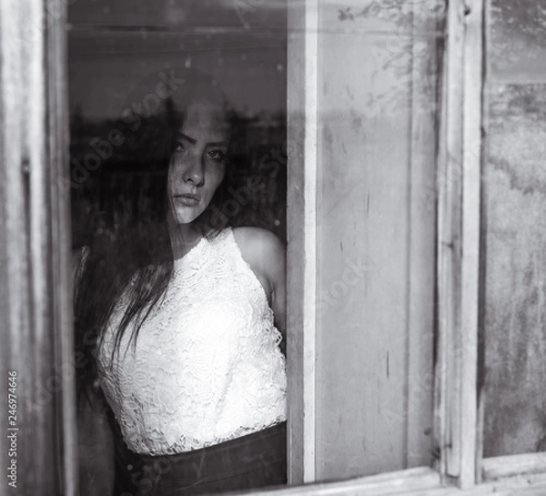 Fototapeta girl by the window in a wooden house with dim light black and white colors