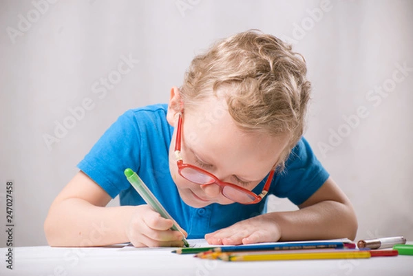 Obraz The boy wears glasses, writes or draws something.