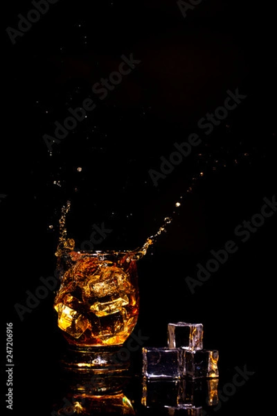 Obraz A glass of whiskey on a beautiful green background and a splash from falling ice