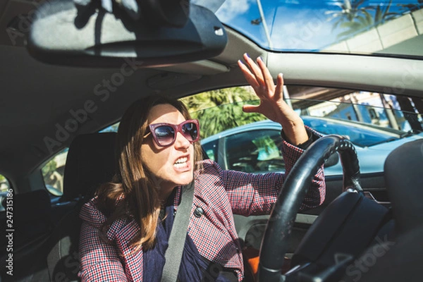 Fototapeta Woman driving screaming stressed in traffic. Girl cursing and screaming at the transit drivers from inside the car passing through stress and hatred