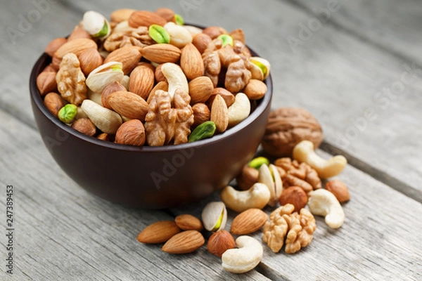 Fototapeta Wooden bowl with mixed nuts on a wooden gray background. Walnut, pistachios, almonds, hazelnuts and cashews, walnut.
