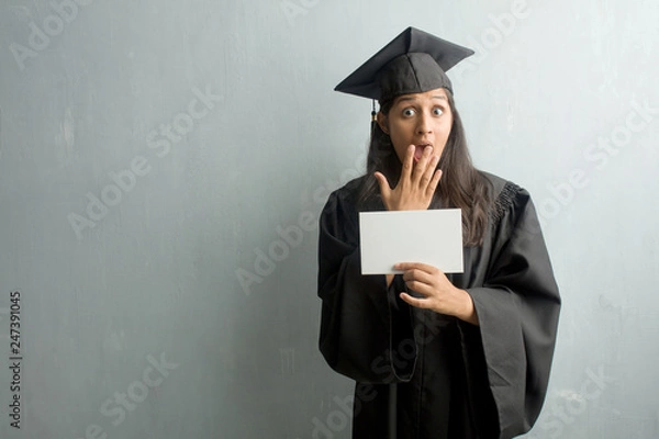 Fototapeta Young graduated indian woman against a wall surprised and shocked, looking with wide eyes, excited by an offer or by a new job, win concept. Holding a placard.