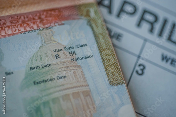 Fototapeta An H-4 visa (immediate family members of the H-1B visa holders) stamp in passport on blurred april calendar background.   H4 visa program deadline concept. Close up view.